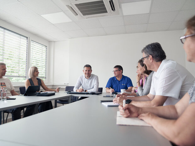 Mitarbeiter:innen des GSZ sitzen gemeinsam in einem Besprechungsraum und führen eine Dienstbesprechung. Alle wirken konzentriert und im Gespräch vertieft.